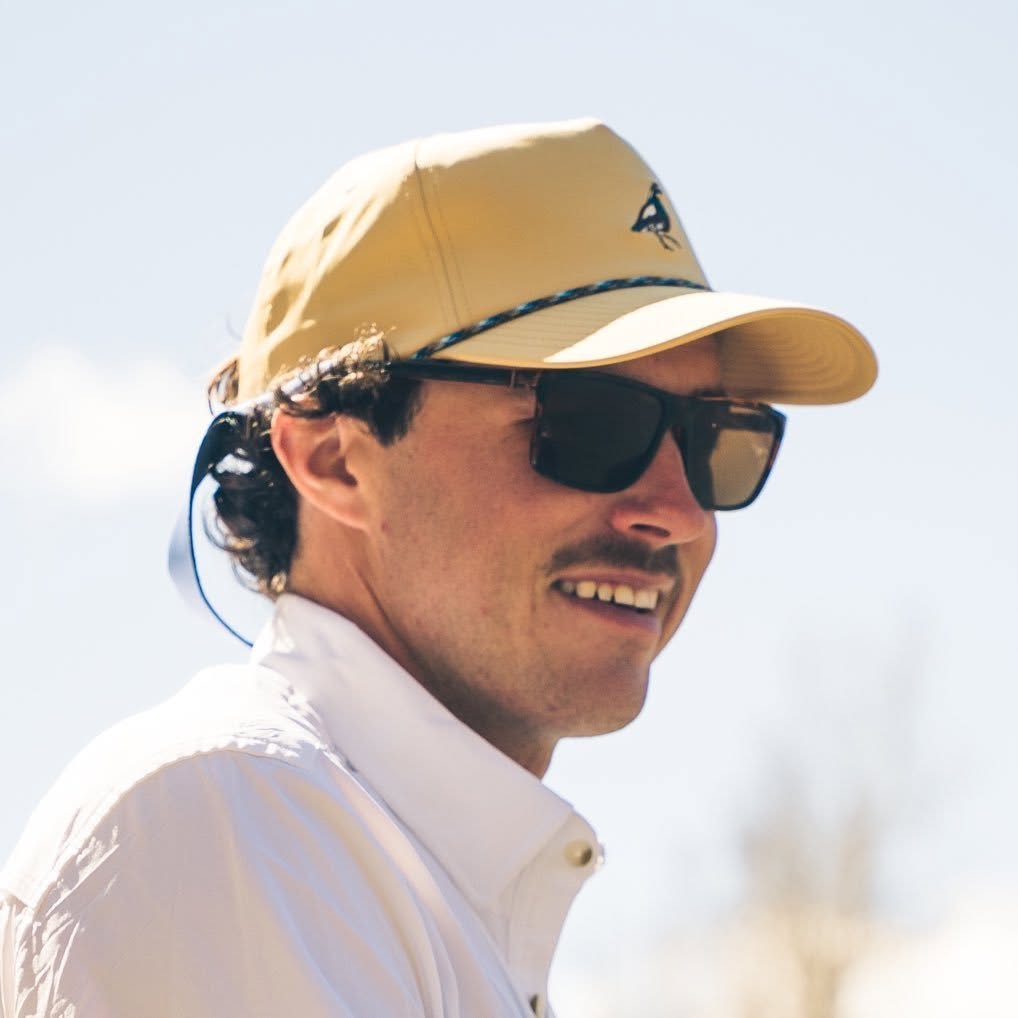 Pierce August in a cap and sunglasses, looking off to the side