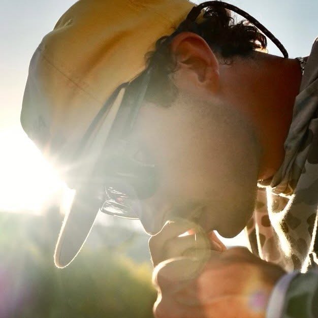 Backlit close-up of Pierce August in a cap and sunglasses at sunset