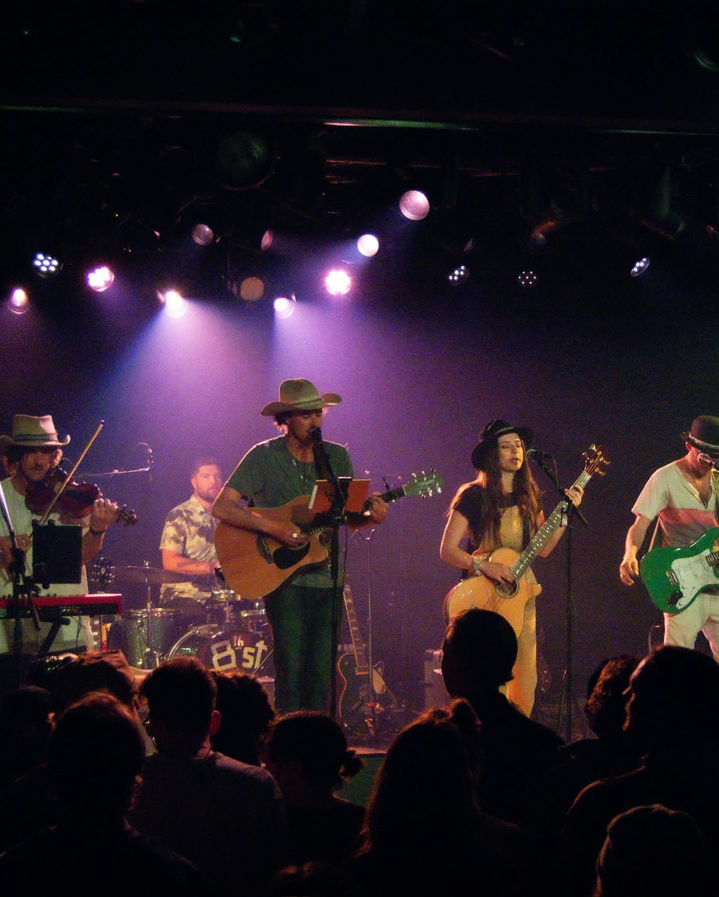 Pierce August performing with his full band on stage under purple lights