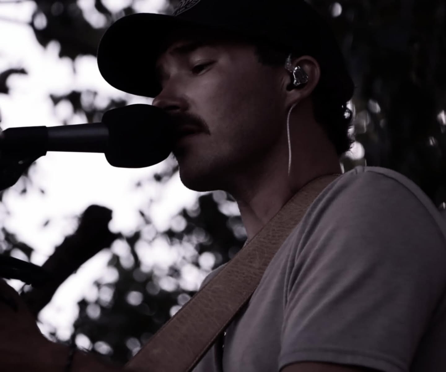 Close portrait of Pierce August singing, backlit under the trees